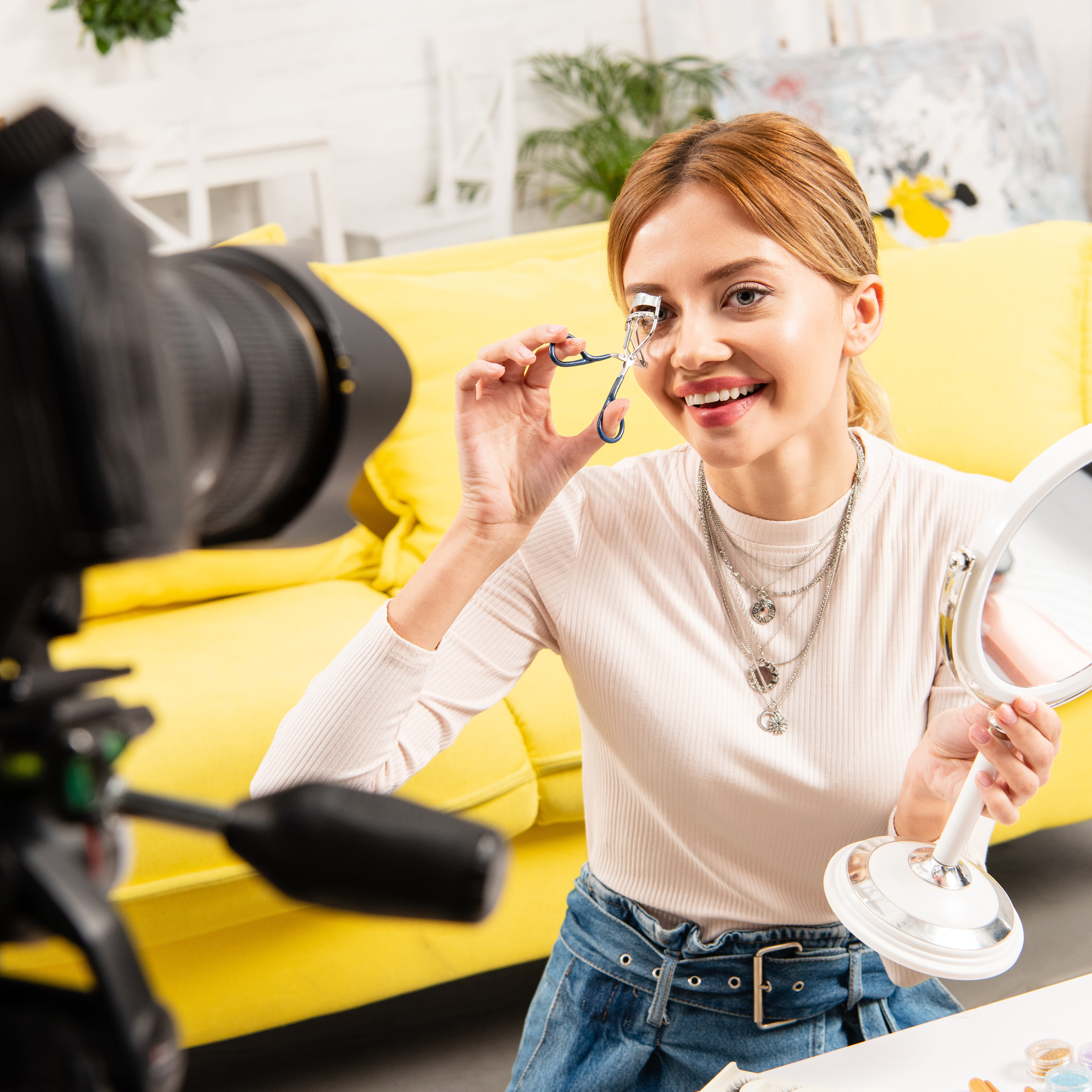 usmievavá beauty blogerka držiaca zrkadlo a natáčajúca si riasy pred videokamerou